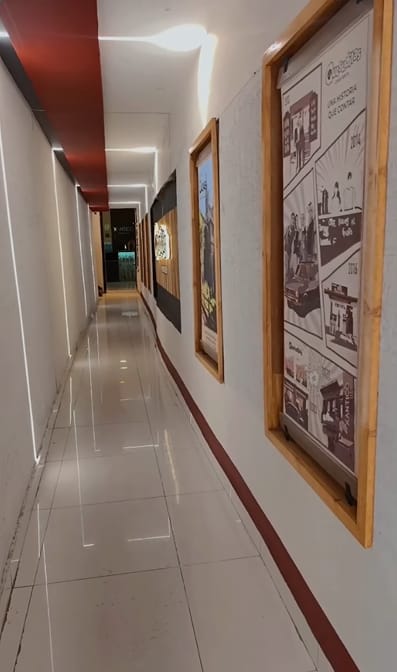 Pasillo largo de piso brillante con cuadros enmarcados en madera a lo largo de la pared y una franja roja en el techo.