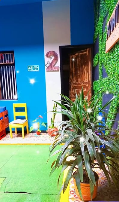 Pared azul intenso del patio con una silla amarilla, plantas en macetas de barro y la puerta número 2.