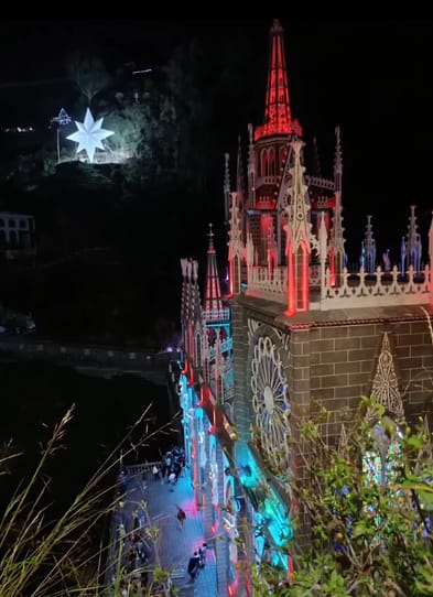 El santuario de Las Lajas de noche, iluminado con luces navideñas rojas, azules y blancas; una gran estrella de luz brilla en la montaña.