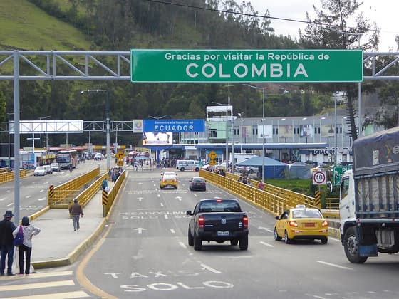 Paso fronterizo de Rumichaca del lado colombiano: un letrero verde dice «Gracias por visitar la República de Colombia» y más adelante se ve el letrero de Ecuador; taxis amarillos en la vía.